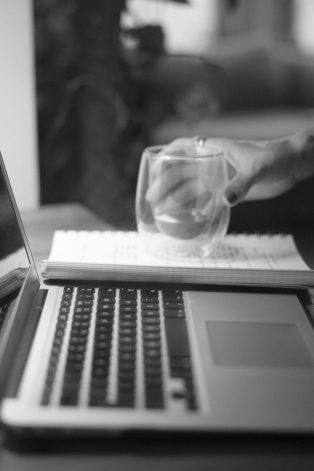 Person working on laptop with a notebook and glass of water in a cozy indoor setting during the late afternoon