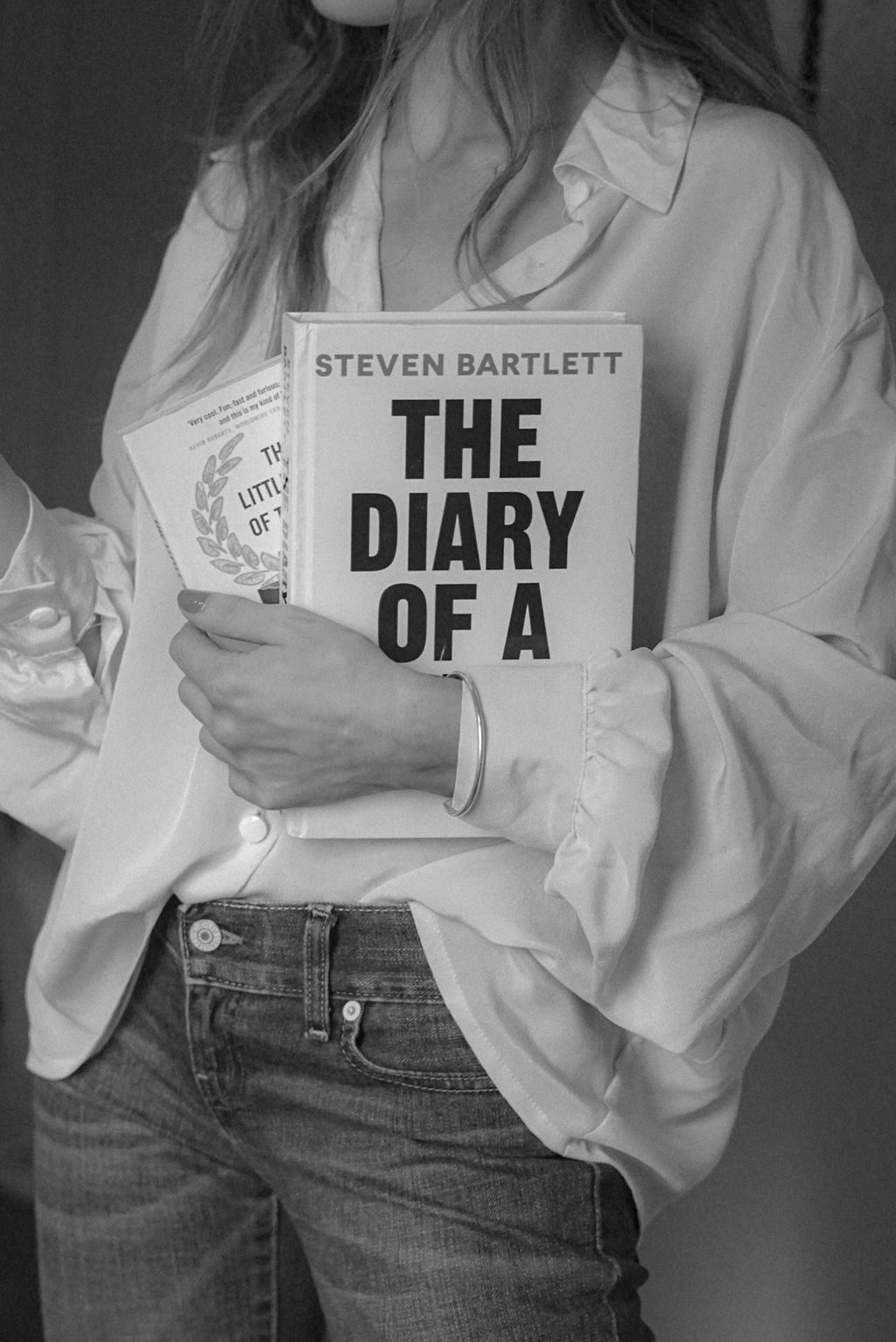 Woman holding books indoors while dressed in a casual outfit during the day